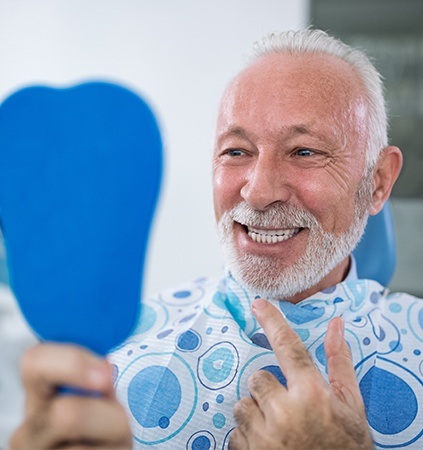 Older man in dental office looking at smile in mirror