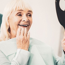 A mature woman looking at her dentures in a mirror