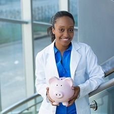 smiling dentist holding pink piggy bank