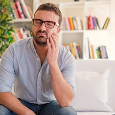man sitting on a couch and holding his face in pain