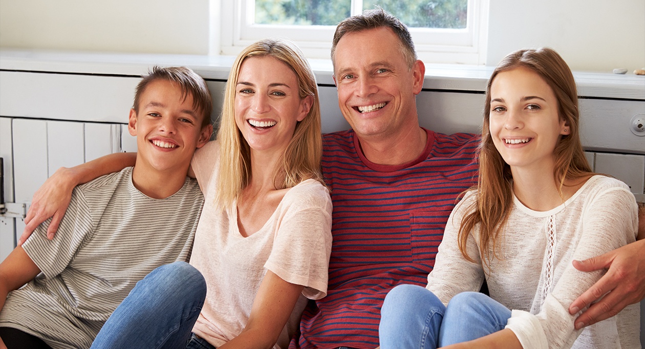 Smiling family of four sitting indoors by a window