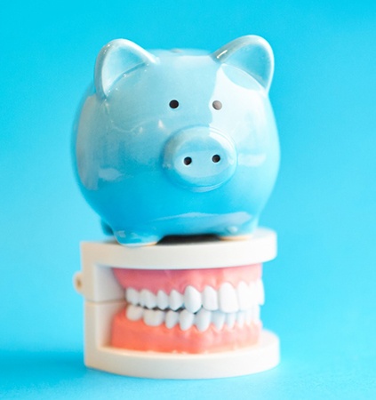 Piggy bank atop model teeth representing cost of Invisalign in Richmond