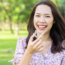 Woman holding Invisalign in Richmond smiling outside
