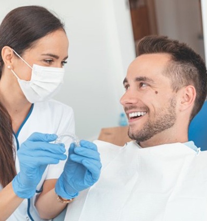 Dentist holding Invisalign in Richmond talks to patient.