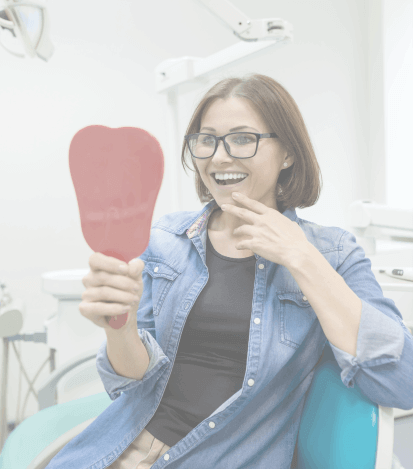 Young woman looking at her smile in a mirror while sitting in dental chair