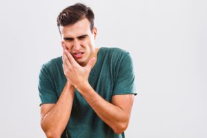 man in green shirt holding mouth in pain