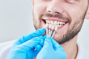 dentist holding veneers up to a patient’s teeth 