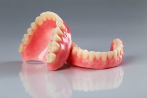 Set of dentures resting against each other in front of a gray background